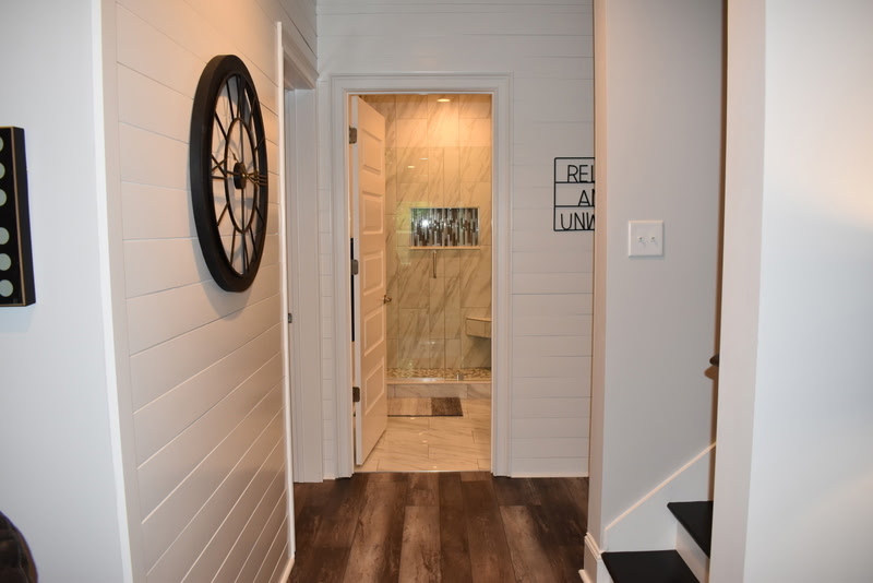 Finished basement hallway with shiplap walls and view of custom shower