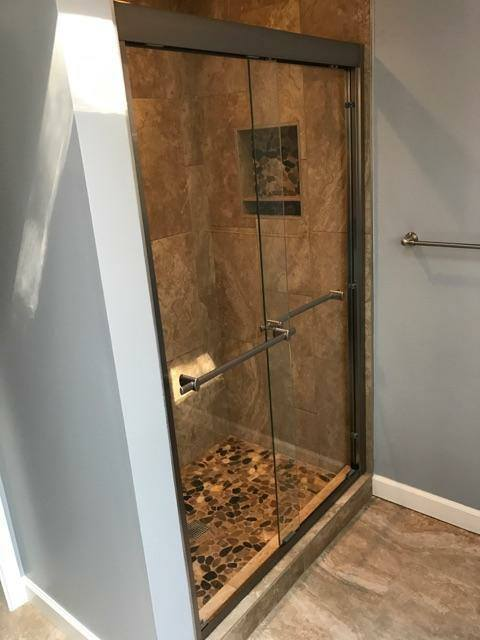Stone tile walk-in shower with glass door and pebble floor