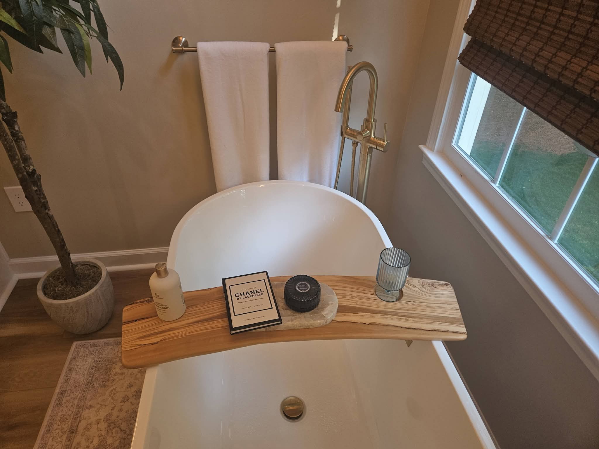 Freestanding soaking tub with gold faucet and wood tub tray