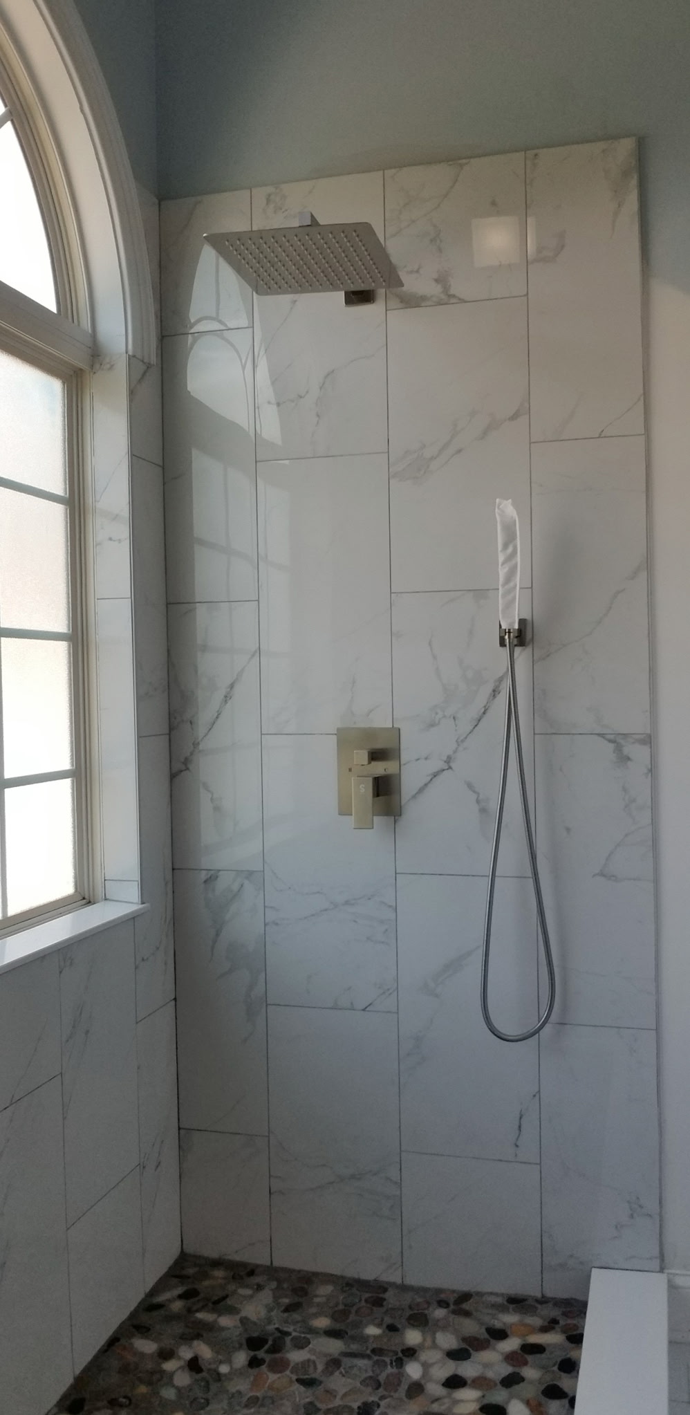 Marble tile walk-in shower with arched window and rain head