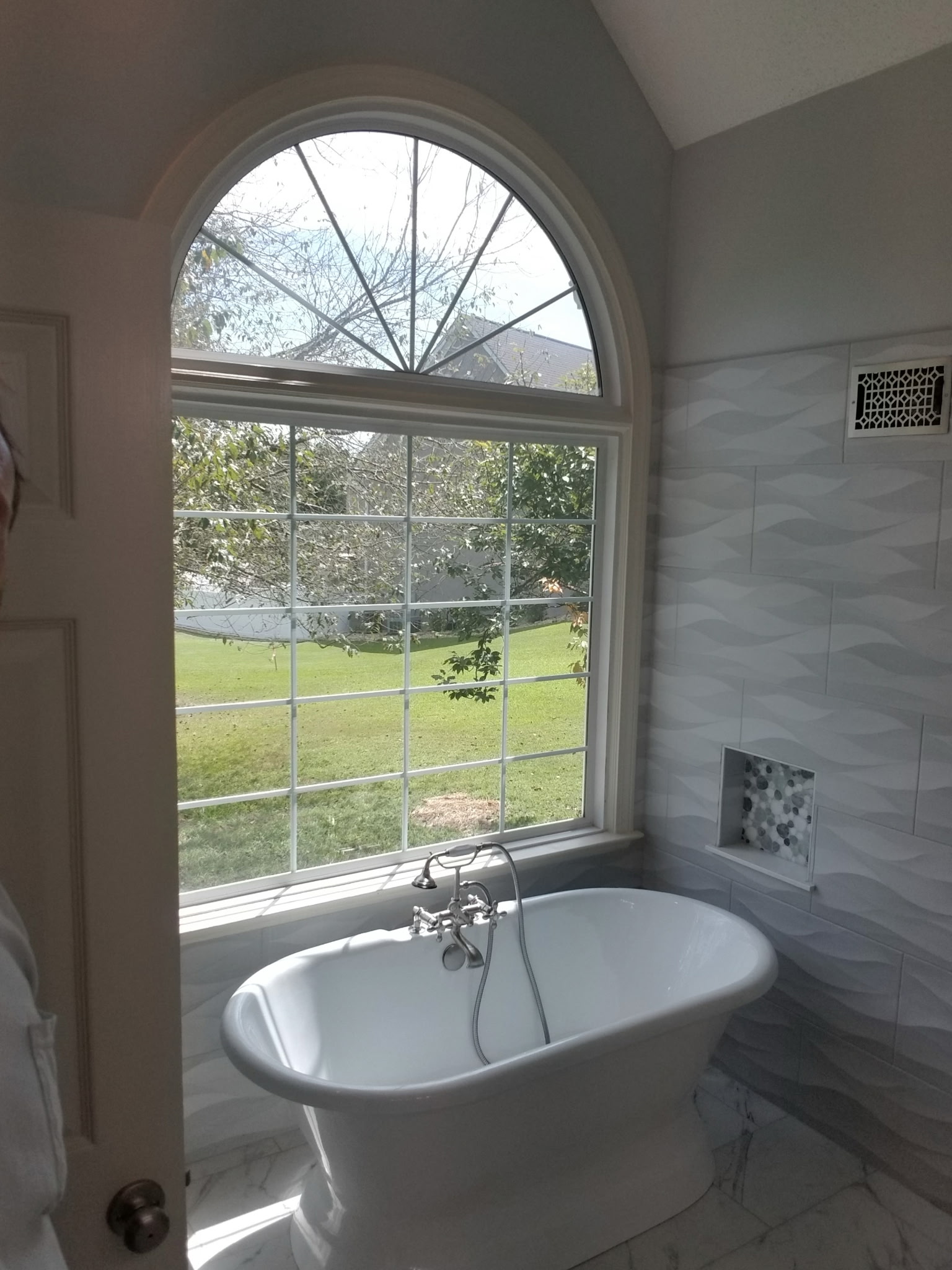 Freestanding soaking tub under arched window with wave tile surround