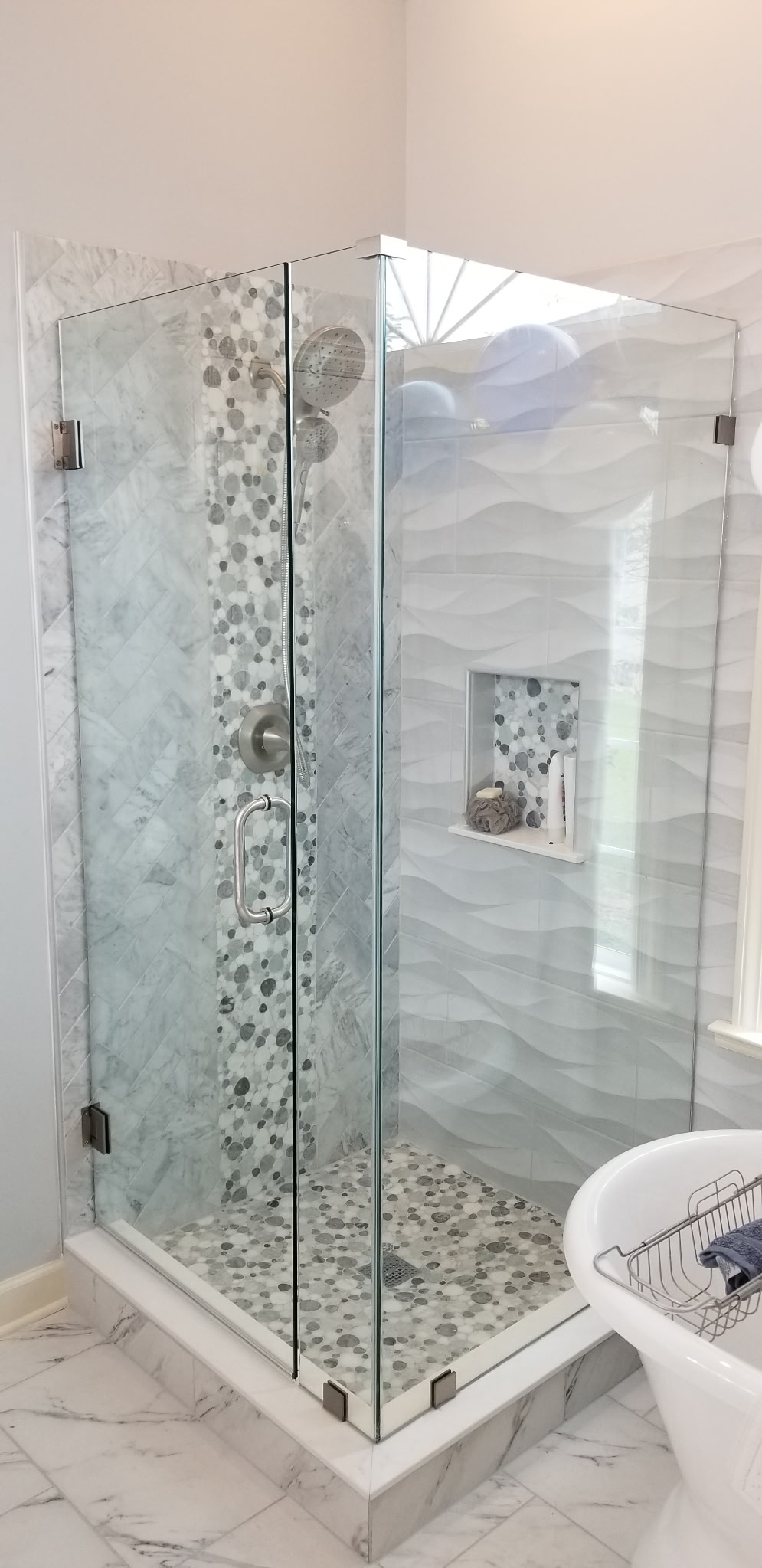 Frameless glass shower with marble herringbone tile and pebble floor