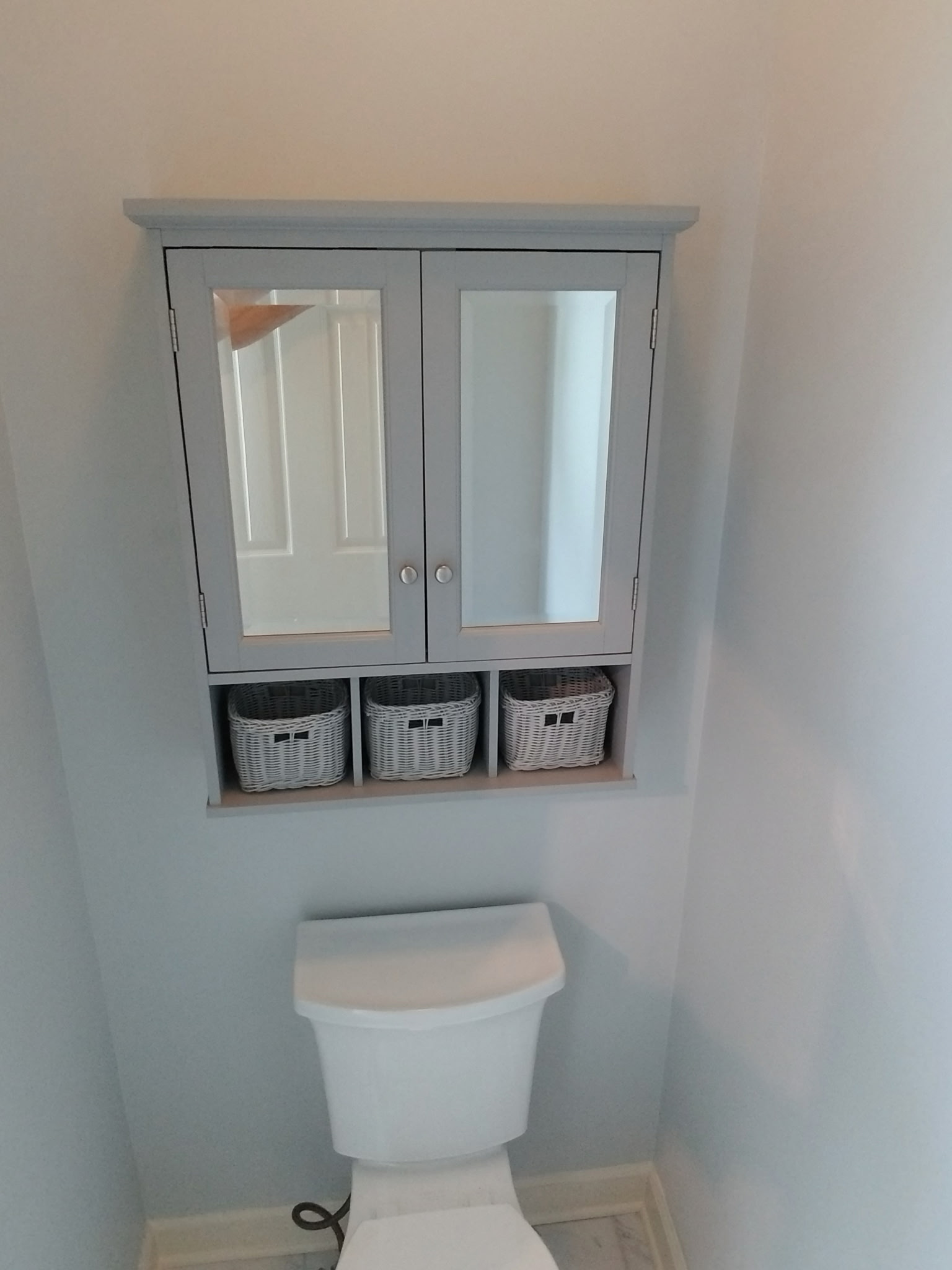 Custom over-toilet storage cabinet with mirrored doors and wicker baskets