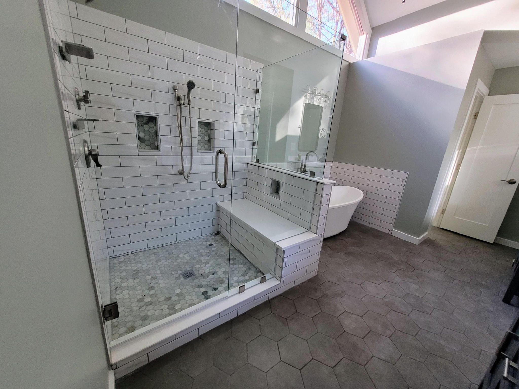 Large glass shower with subway tile bench and freestanding tub