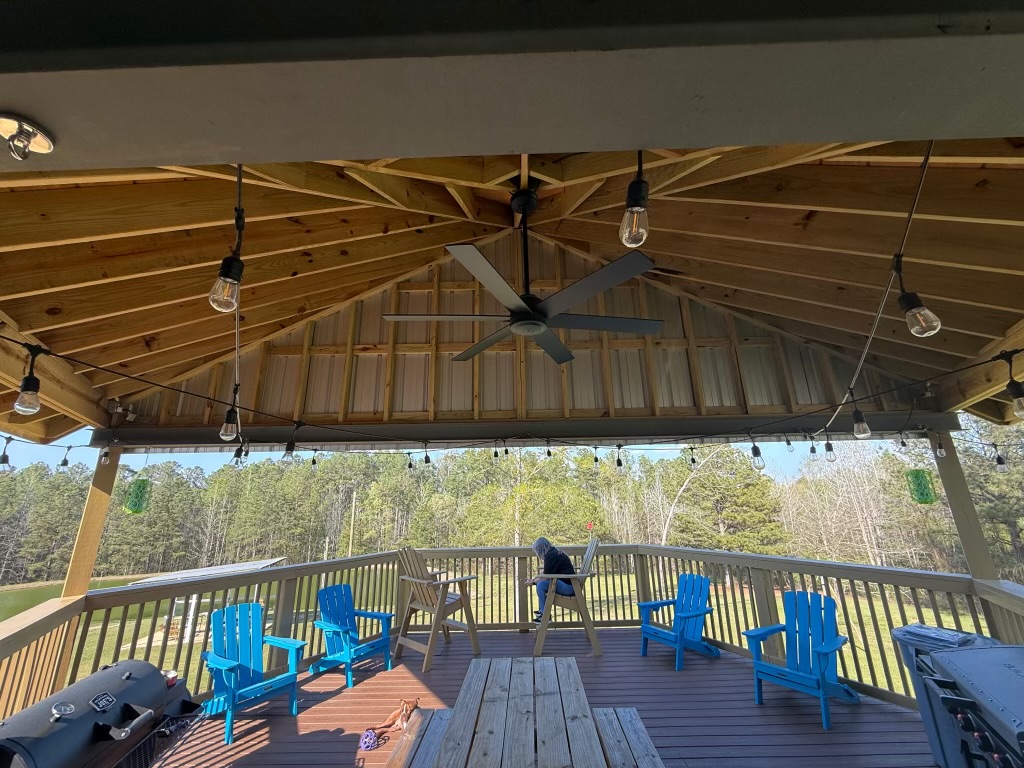 Covered deck pavilion with string lights, ceiling fan and Adirondack chairs overlooking wooded property