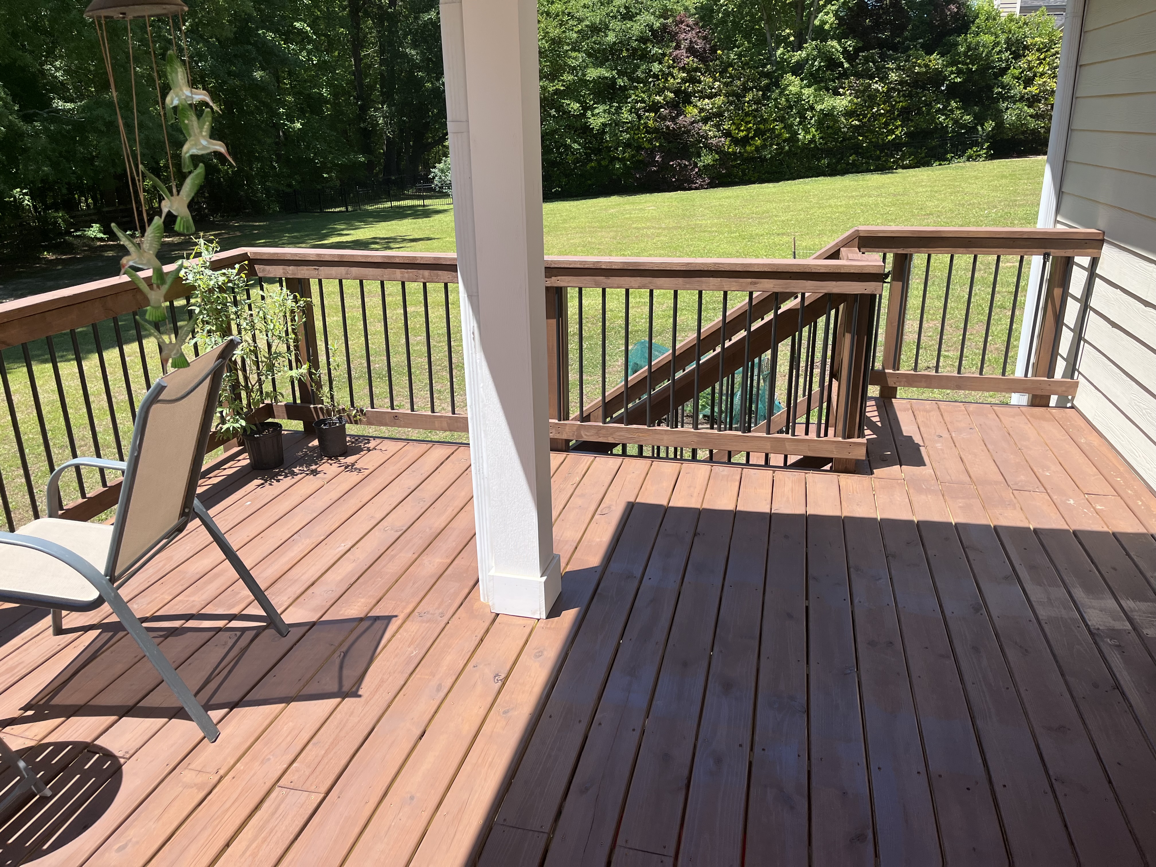 Spacious stained deck with black metal balusters and wooded backyard view