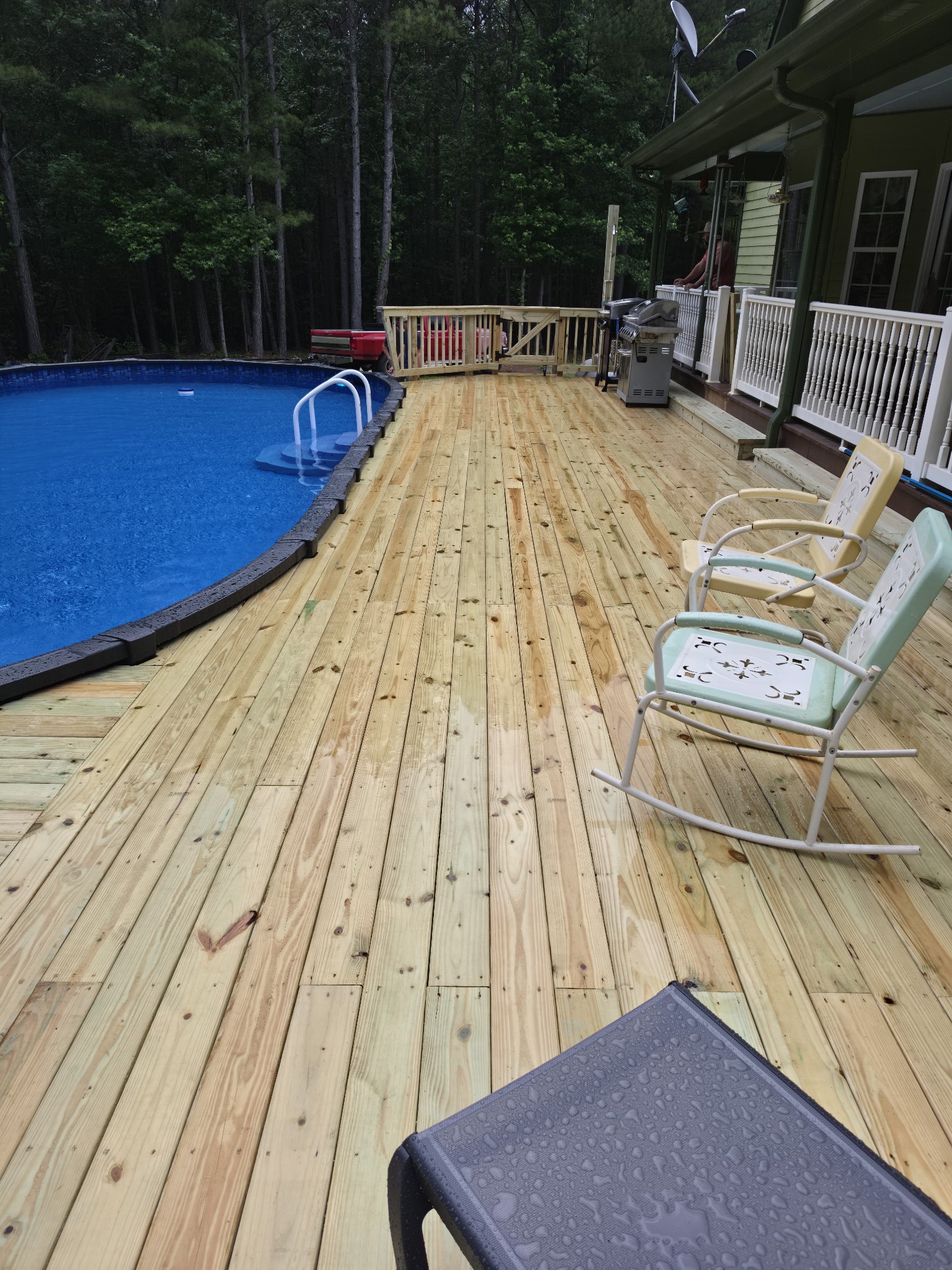 Large pool deck with above-ground pool and wooded backyard
