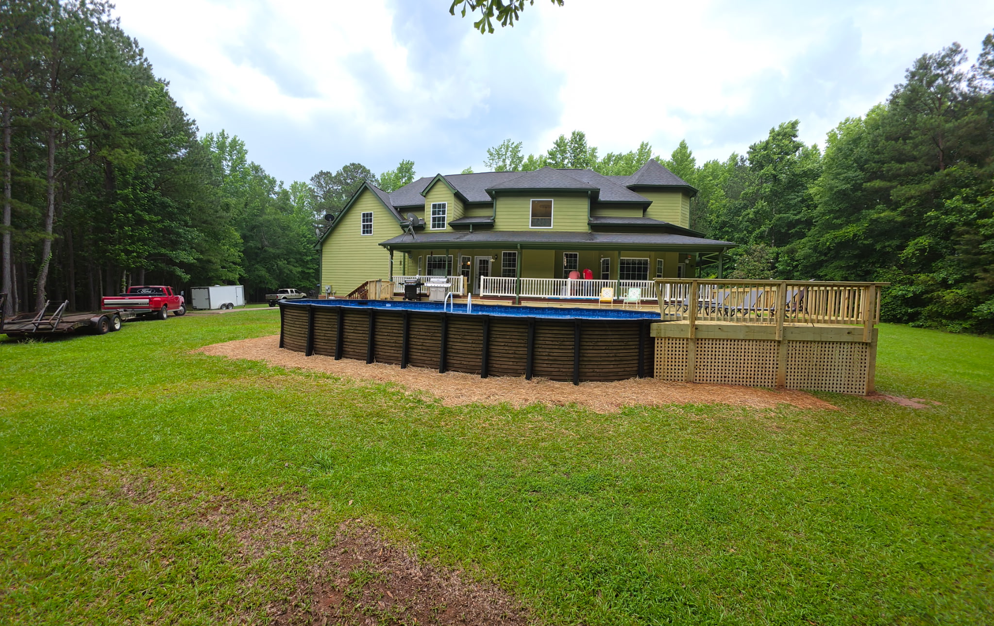 Full rear view of new deck with above-ground pool and green home